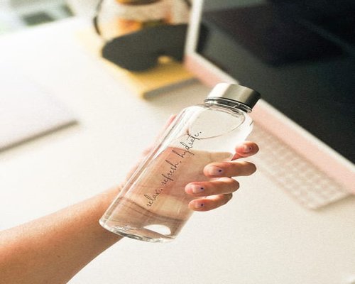 Person holding a reusable water bottle in a home office setup